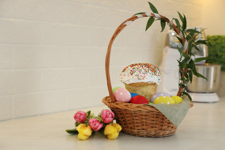 Basket with traditional Easter cake, dyed eggs and flowers on table near white brick wall. Space for textの写真素材