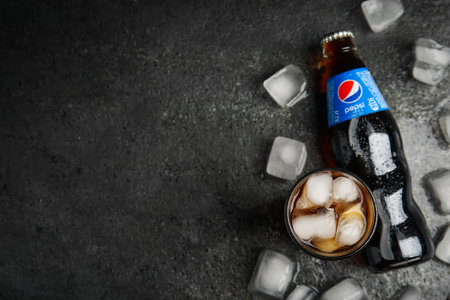 MYKOLAIV, UKRAINE - FEBRUARY 11, 2021: Glass of Pepsi, bottle and ice cubes on gray table, flat lay. Space for textのeditorial素材