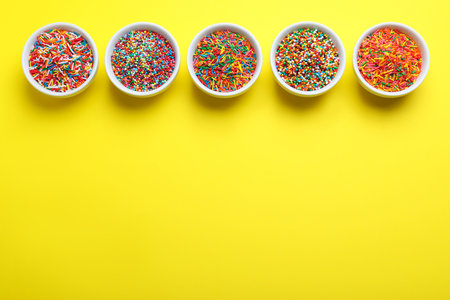 Colorful sprinkles in bowls on yellow background, flat lay with space for text. Confectionery decorの写真素材