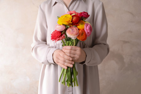 Woman holding beautiful ranunculus flowers against beige background, closeupの写真素材