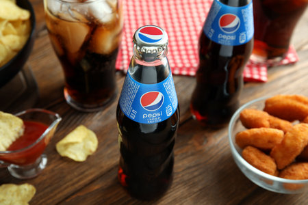 MYKOLAIV, UKRAINE - FEBRUARY 16, 2021: Glass bottles of Pepsi and snacks on wooden tableのeditorial素材