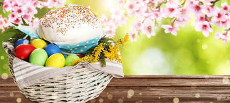 Basket with traditional Easter cake, eggs and flowers on wooden table outdoors, space for text....