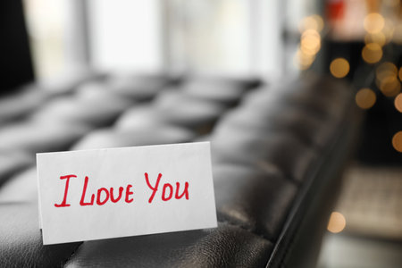 Paper with text I Love You on sofa against festive lights, closeupの写真素材