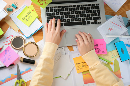 Woman using laptop at messy table, top view. Concept of being overwhelmed by work