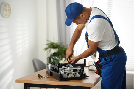 Repairman with screwdriver fixing modern printer in officeの写真素材