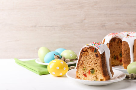 Piece of glazed Easter cake with sprinkles and painted eggs on white wooden table, space for text
