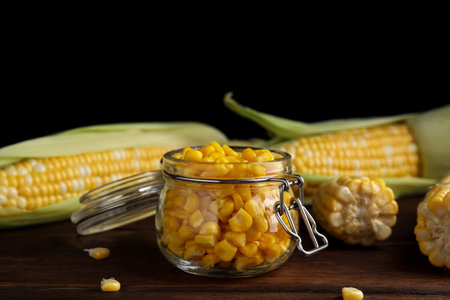 Tasty sweet corn kernels in jar and fresh cobs on wooden tableの写真素材