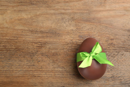 Sweet chocolate egg with green bow on wooden table, top view. Space for textの写真素材