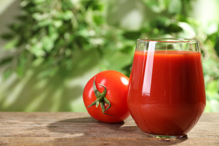 Delicious juice in glass and fresh tomato on wooden table against blurred background, space for textの写真素材