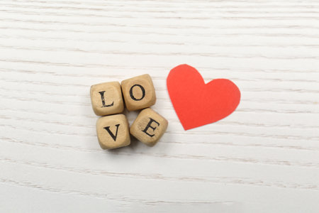 Mini cubes with letters forming word Love near red paper heart on white wooden background, flat layの写真素材