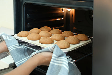 Woman taking cupcakes out of oven indoors, closeup