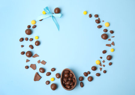 Frame of delicious chocolate Easter egg and candies on light blue background, flat lay. Space for textの写真素材