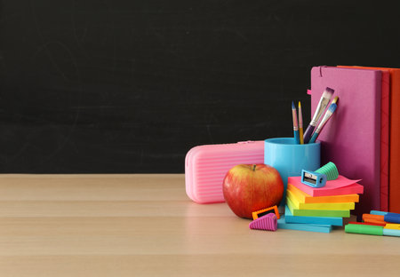 Different school stationery on wooden table near blackboard, space for text. Back to schoolの写真素材