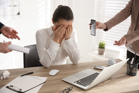 Stressed and tired young woman surrounded by colleagues at workplace, closeupの写真素材
