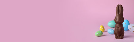 Chocolate Easter bunny and dyed eggs on pink background. Space for text