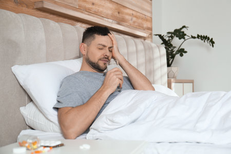Man taking medicine for hangover in bed at homeの写真素材