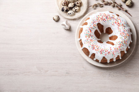 Glazed Easter cake with sprinkles, decorative bunny, quail eggs and willow branches on white wooden table, flat lay. Space for textの写真素材