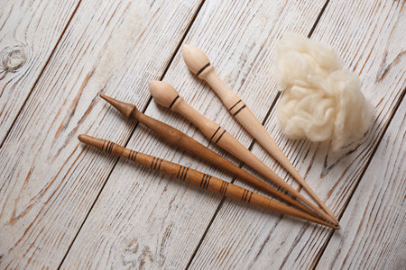 Soft wool and spindles on white wooden table, flat lay