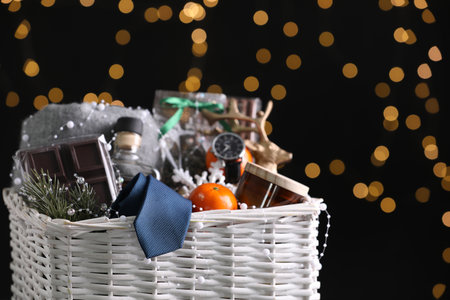 Wicker basket with Christmas gift set on black background against festive lightsの写真素材