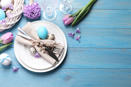 Festive Easter table setting with  painted eggs and floral decor on light blue wooden background,...