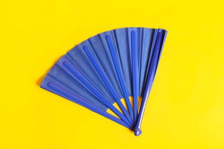 Blue hand fan on yellow background, top viewの写真素材
