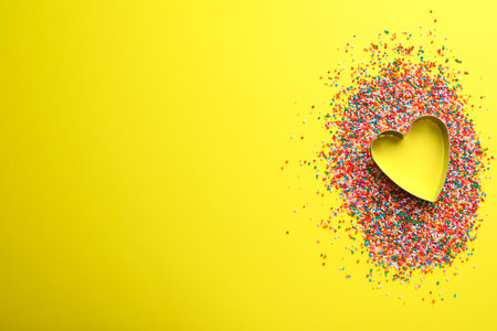 Heart shaped cookie cutter and sprinkles on yellow background, flat lay with space for text. Confectionery decorの写真素材