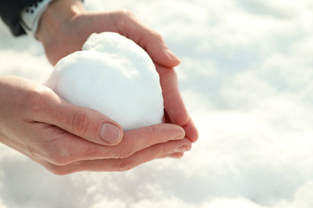 Woman holding heart made of snow outdoors, closeup. Space for textの写真素材
