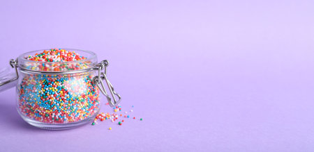 Colorful sprinkles in jar on lilac background, space for text. Confectionery decorの写真素材