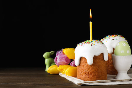 Traditional Easter cakes and one with burning candle on wooden table against black background. Space...