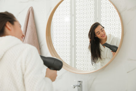 Beautiful young woman using hairdryer in bathroomの写真素材