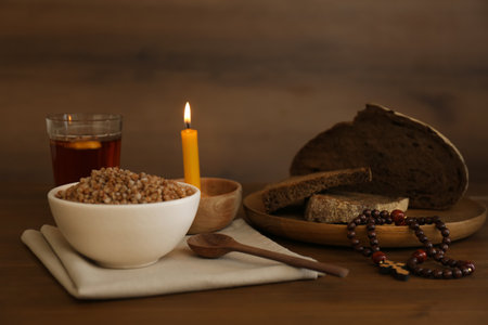 Buckwheat porridge, spoon, rosary beads, bread and candle on wooden table. Lent seasonの写真素材