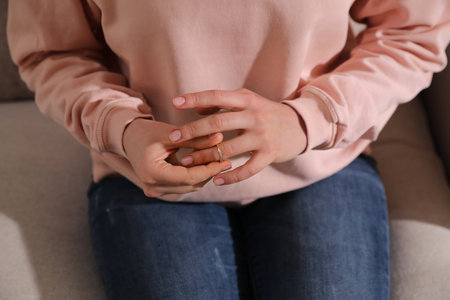 Woman taking off wedding ring on sofa, closeup. Divorce conceptの写真素材