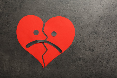 Broken heart with sad face on gray background, flat lay. Space for text