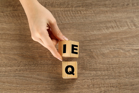 Woman turning cube with letters E and I near Q at wooden table, top view. Space for textの写真素材