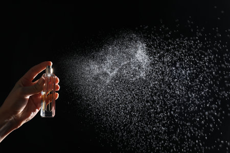 Woman spraying luxury perfume on black background, closeup