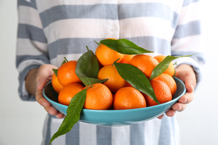 Woman holding plate with fresh tangerines on light background, closeupの写真素材