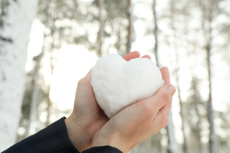 Woman holding heart made of snow outdoors, closeupの写真素材