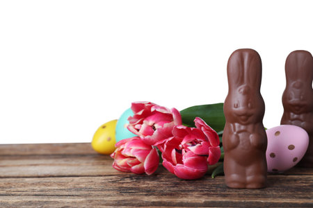 Chocolate Easter bunnies, eggs and tulips on wooden table against white background. Space for textの写真素材
