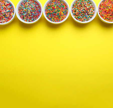 Colorful sprinkles in bowls on yellow background, flat lay with space for text. Confectionery decorの写真素材