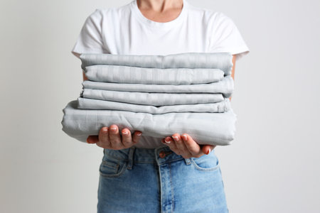 Woman holding stack of clean bed linens on light gray backgroundの写真素材