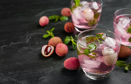 Delicious lychee cocktails with mint and fresh fruits on black table. Space for textの写真素材