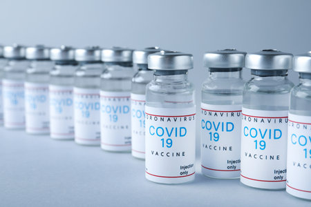 Vials with coronavirus vaccine on light gray background