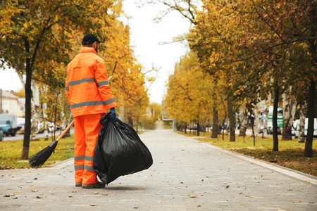 Street cleaner with broom and garbage bag outdoors on autumn day, back viewの写真素材