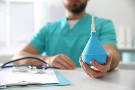 Doctor holding light blue enema at table in hospital, closeupの写真素材