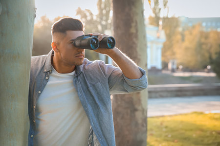 Jealous man with binoculars spying on ex girlfriend in parkの写真素材