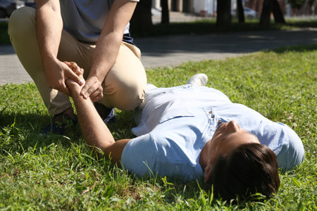 Passerby checking pulse of unconscious man outdoors. First aid