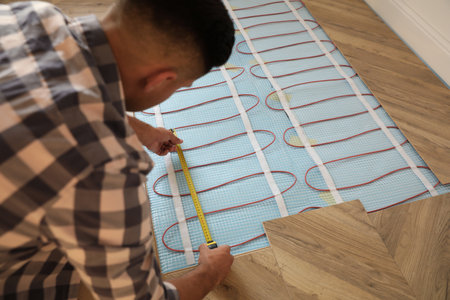Professional worker installing electric underfloor heating system indoorsの写真素材