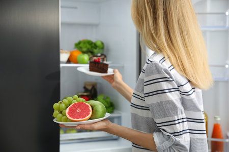 Choice concept. Woman taking plates with fruits and cake from refrigerator in kitchen, closeupの写真素材