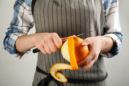 Woman peeling fresh orange with knife on light gray background, closeupの写真素材