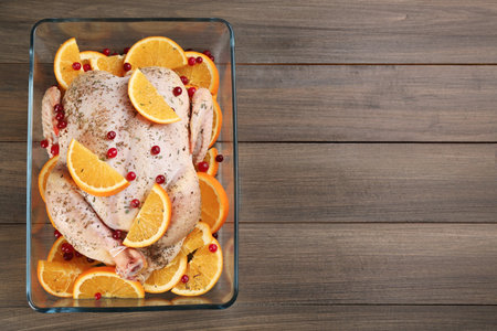 Raw chicken with orange slices and cranberries on wooden table, top view. Space for textの写真素材